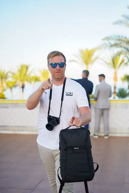 Miembro del equipo de DKZ Studio con cámara y mochila junto a un paseo marítimo con palmeras · marketing y producción audiovisual para Alicante