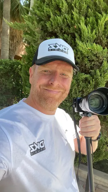 Videógrafo de DKZ Studio con cámara profesional sobre monopié y gorra del estudio · agencia de marketing y vídeo para negocios de La Manga